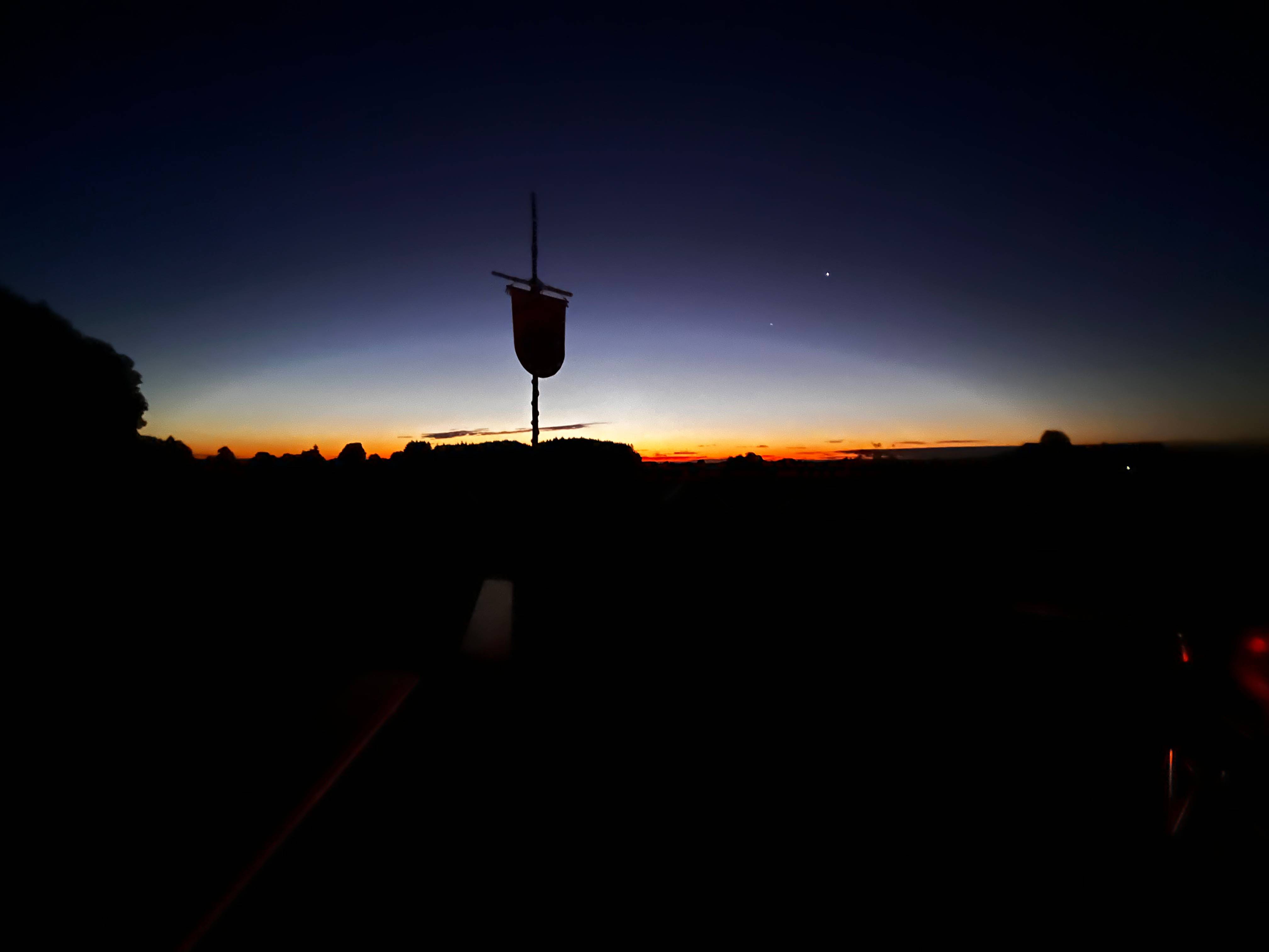 Silhouette eines Mastes mit Beutel vor einem farbenfrohen Sonnenuntergang am Zeltplatz des Boni-Arche-Camps.