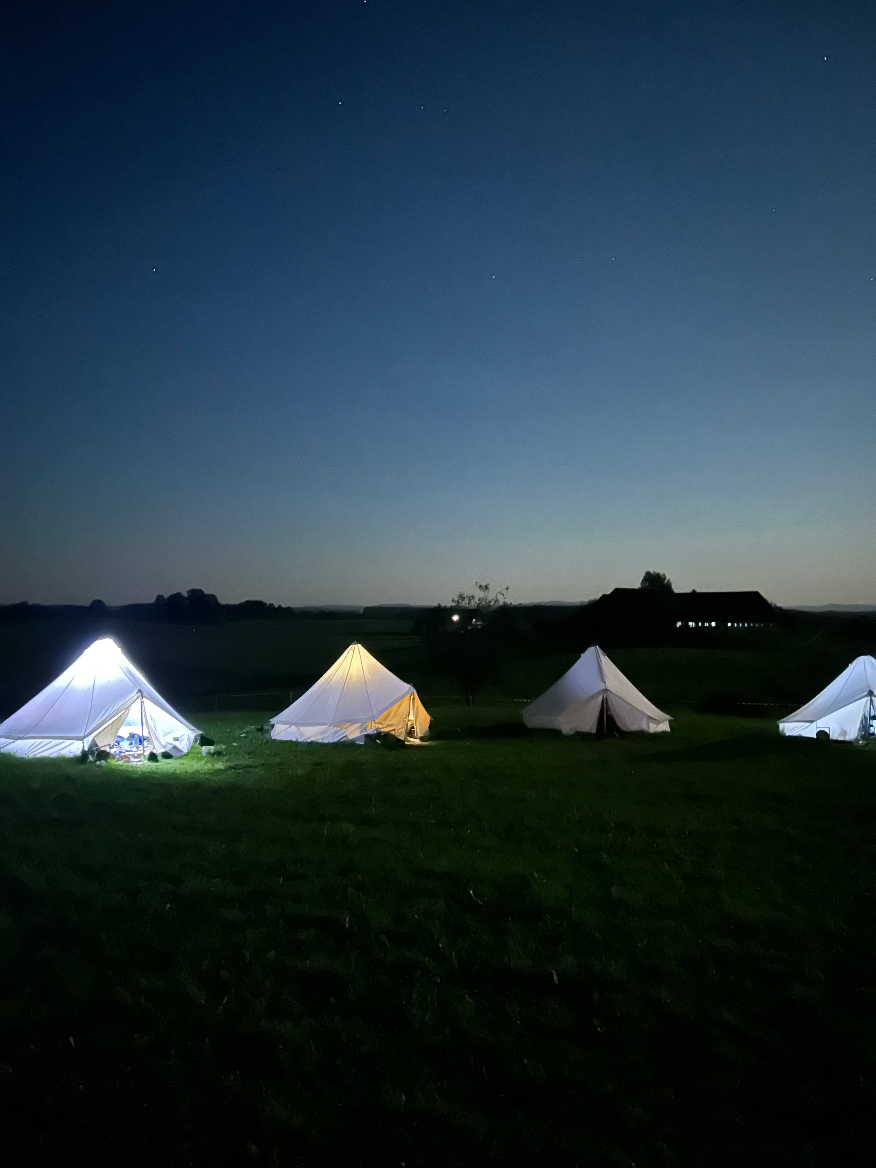 Beleuchtete Zelte auf der Wiese des Boni-Arche-Camps unter einem sternenklaren Nachthimmel.