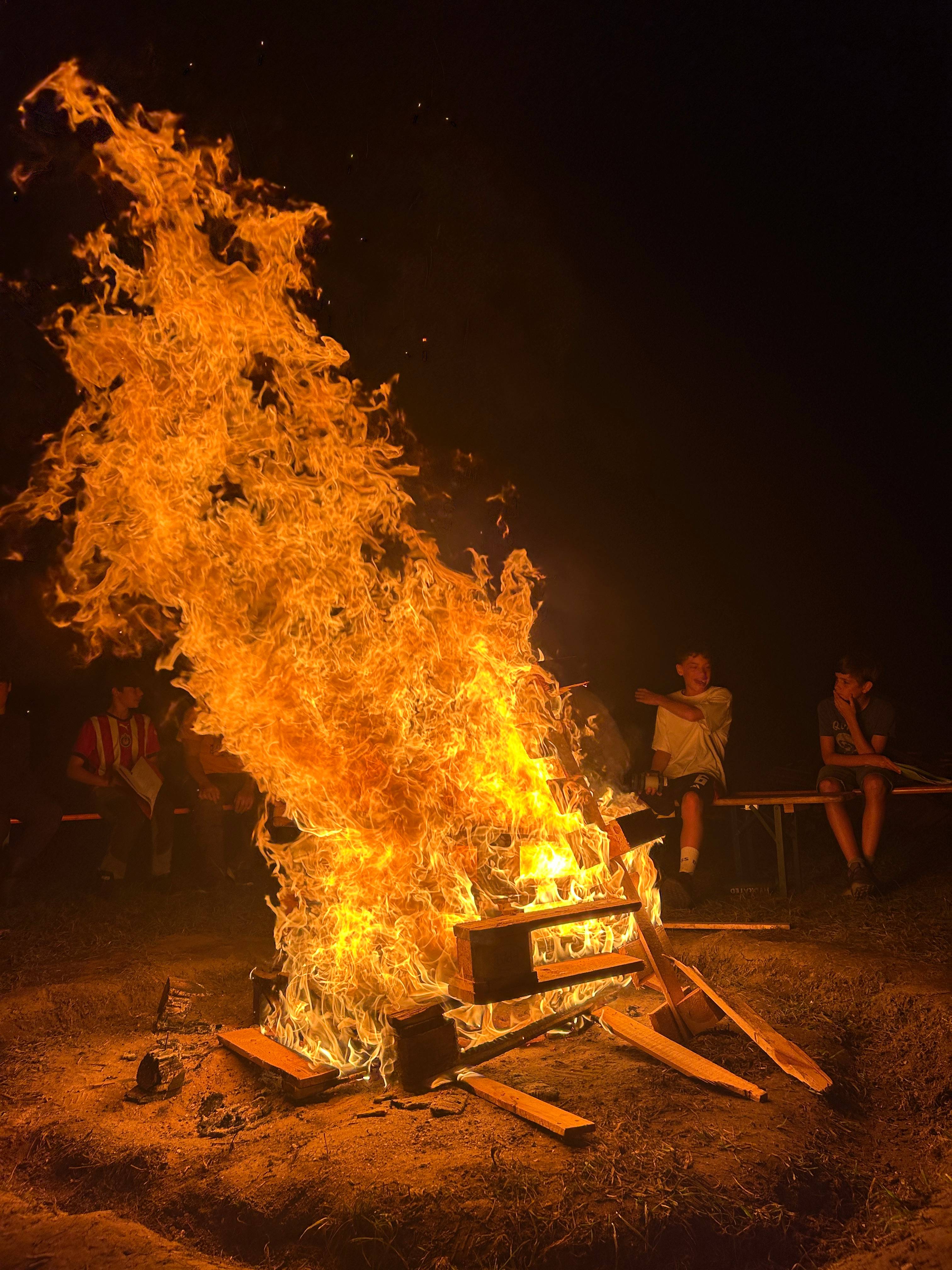 Jugendliche sitzen abends um ein prasselndes Lagerfeuer im Zeltlager und genießen die warme Atmosphäre.
