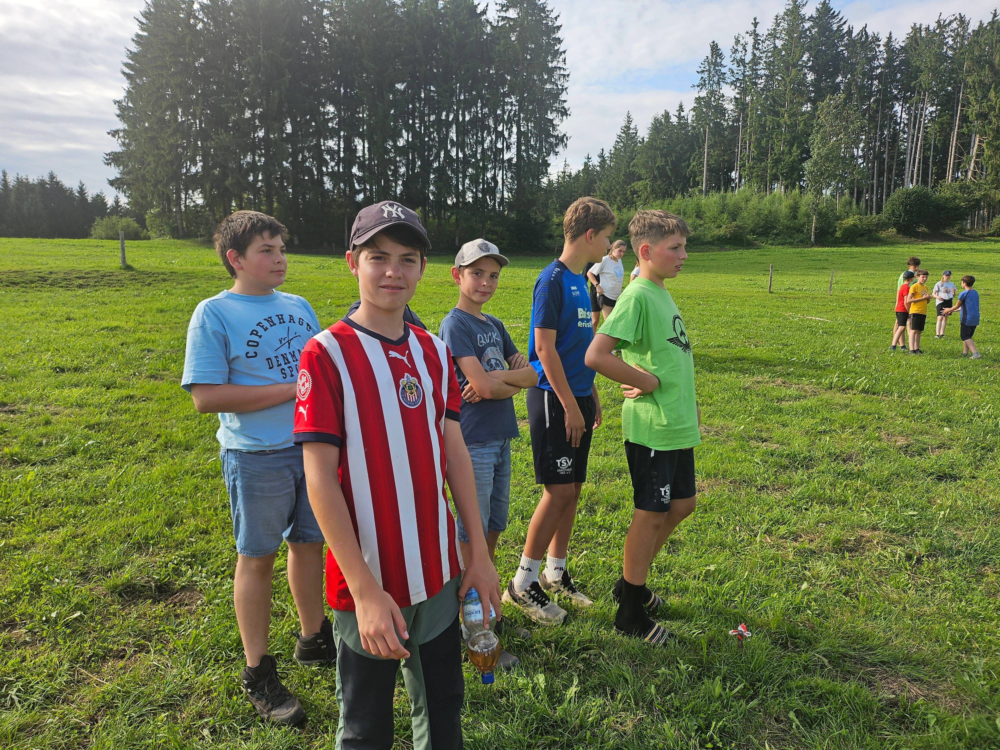 Kinder beim Freiluftspiel auf der Wiese des Boni-Arche-Camps, im Hintergrund Wald und weitere Teilnehmer.
